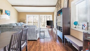 A spacious living room with a gray sofa, wooden dining table, and a TV. - Cutest place ever! Fun Airline decor will make you smile! Huge deck! (Jasper)