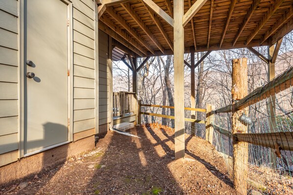 A covered outdoor area with a wooden structure, a fenced area, and a building with siding.