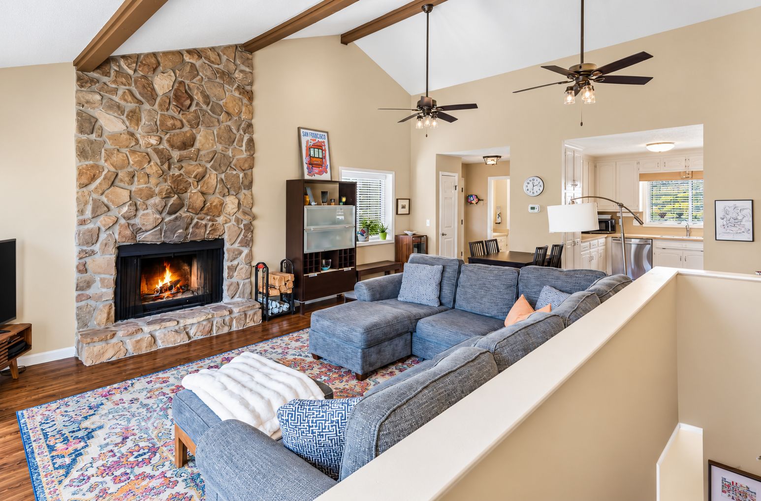 A living room with a stone fireplace, a sectional sofa, a television, and a ceiling fan.