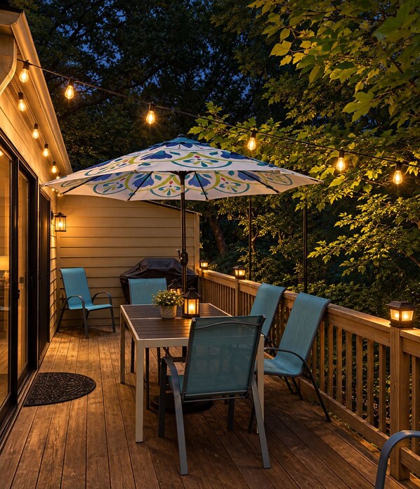 An outdoor deck with a table and chairs, a grill, string lights, and an umbrella.