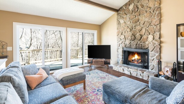 A living room with a stone fireplace, a large window with a view of trees, and a flat-screen TV. - Cutest place ever! Fun Airline decor will make you smile! Huge deck! (Jasper)