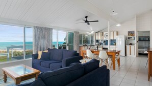 A modern living room with a large sofa, a coffee table, and a view of the ocean. - Wave and See - 53 Gold Coast Drive (Carrickalinga)
