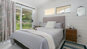A bedroom with a bed, bedside tables, a nightstand, a window, and a view of the outdoors. - Wave and See - 53 Gold Coast Drive (Carrickalinga)