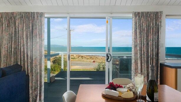 A room with a view of the ocean, a table with cheese and wine, and a blue sofa. - Wave and See - 53 Gold Coast Drive (Carrickalinga)