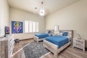 A bedroom with two wooden beds, a desk, a chair, a dresser, and artwork on the walls.