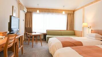A hotel room with a bed, a desk with a television, a seating area, and a window with curtains.