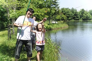 A group of people fishing by a calm river surrounded by greenery.