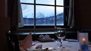 A table set for dining with a candle, a glass, and a view of mountains through a window. - Sahoro Resort Hotel (Shintoku)