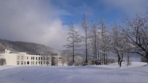 A snow-covered landscape with a building featuring multiple windows and a gate. - Sahoro Resort Hotel (Shintoku)