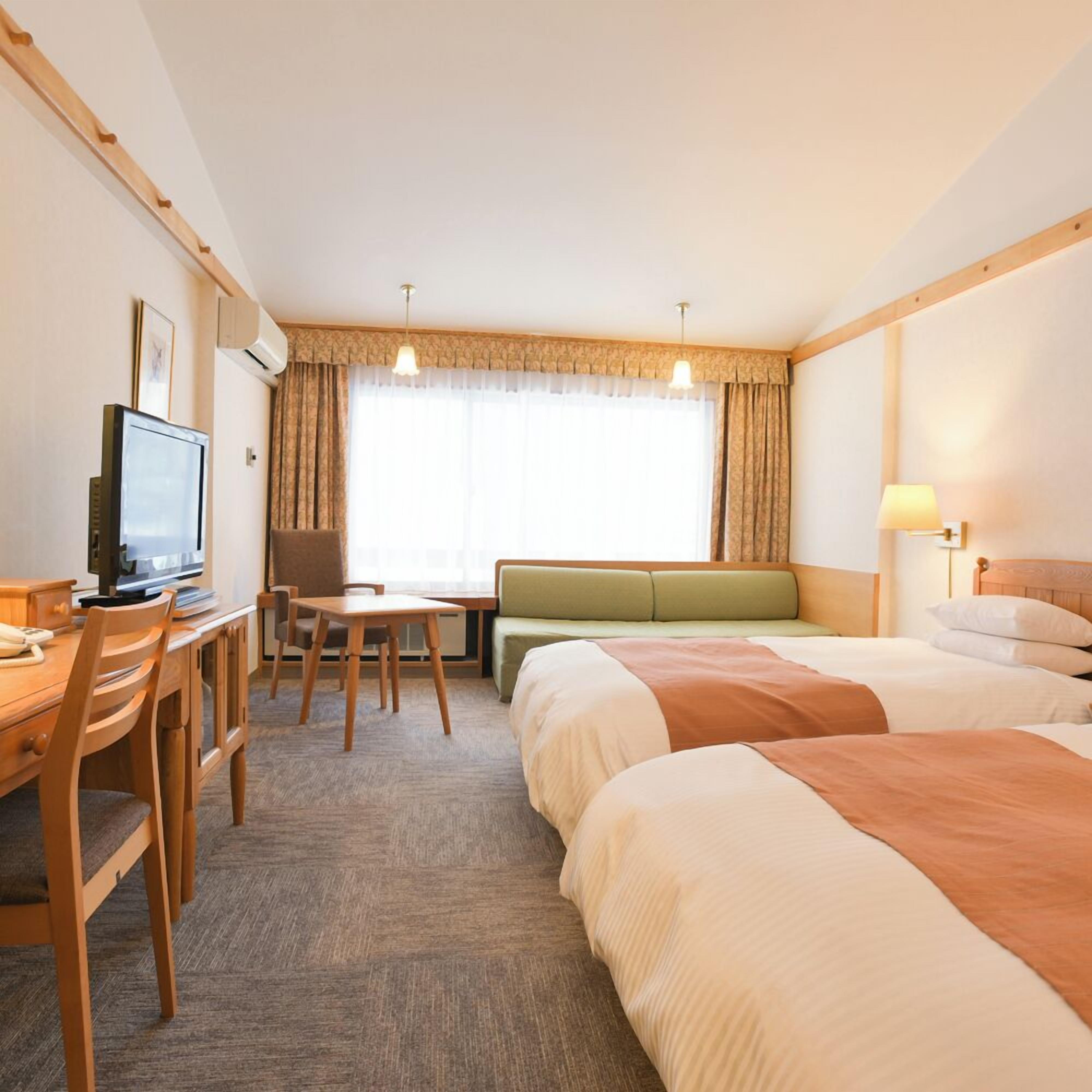 A hotel room with a desk, a television, a sofa, and two beds.