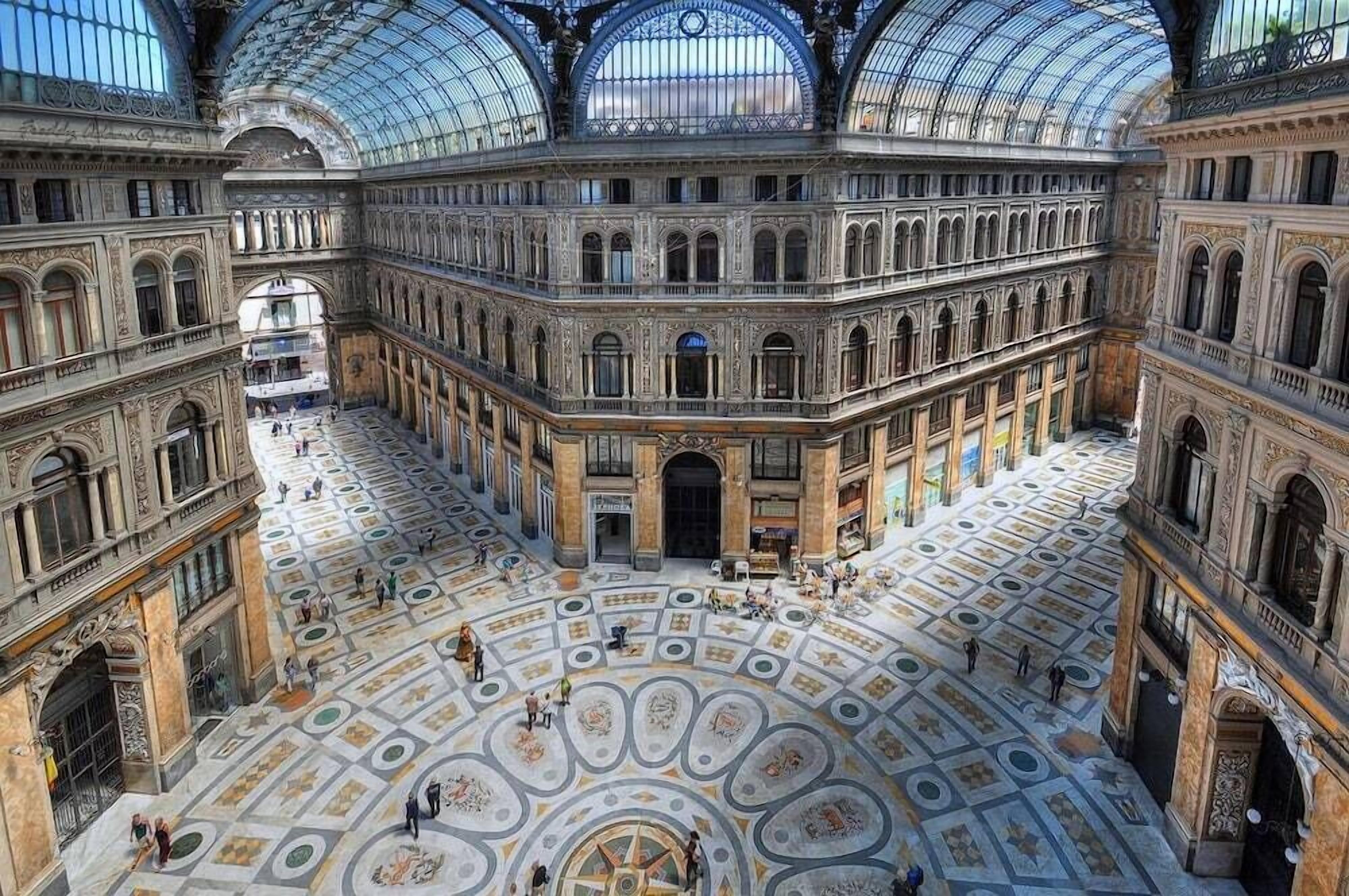 Un imposant bâtiment historique doté d’une vaste cour intérieure, d’une architecture richement décorée et d’un plafond en forme de dôme de verre.