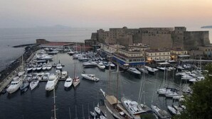A marina with numerous boats docked, a historic fort, and buildings along the waterfront. - Up Hotel (Naples)