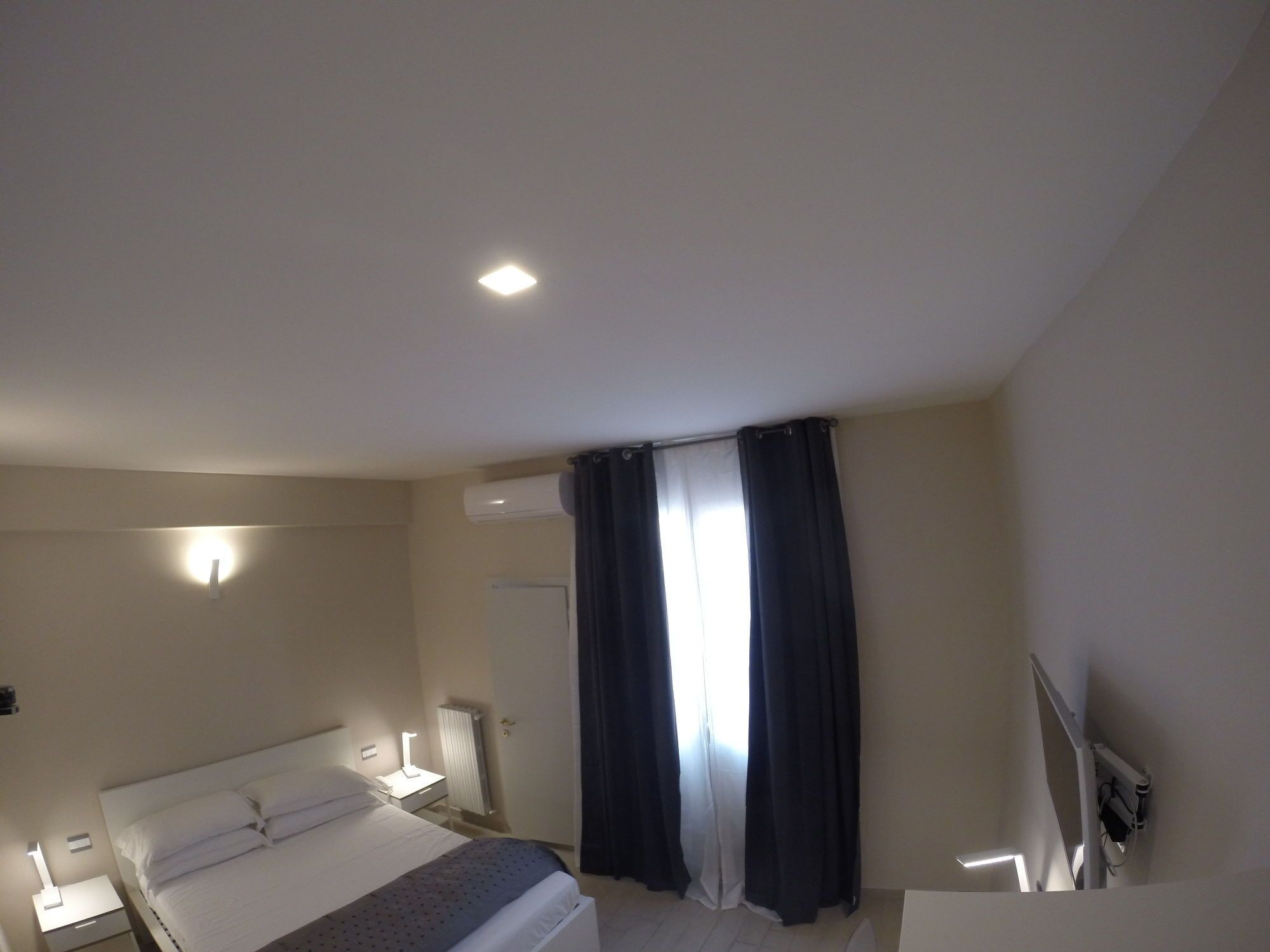 Habitació d'hotel amb un llit, taules de nit, escriptori, cadira, finestra amb cortines i llum al sostre.