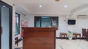 A reception area with a wooden desk, chairs, a television, and a potted plant. - Reddoorz @ Buah Batu (Bandung)
