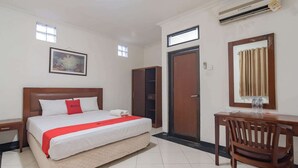 A hotel room with a bed, a desk, a chair, a wardrobe, a painting, and an air conditioning unit. - Reddoorz @ Buah Batu (Bandung)