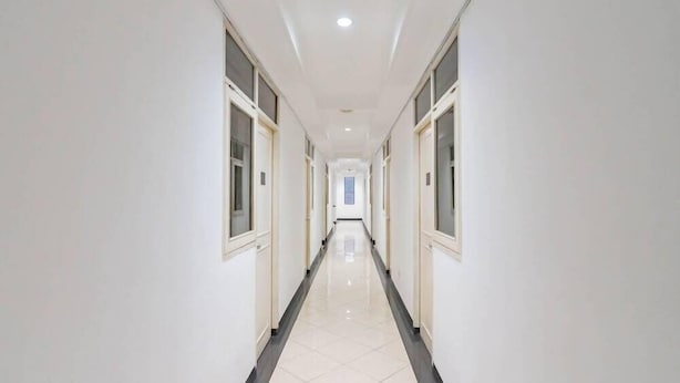 A long, narrow hallway with white walls and a tiled floor, leading to a door at the end. - Reddoorz @ Buah Batu (Bandung)