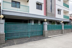 A residential building with a covered parking area, a green metal fence, and a concrete wall. - Reddoorz @ Buah Batu (Bandung)