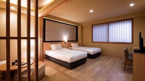 Habitación de hotel con dos camas, un escritorio, una silla y un ventanal con persianas.