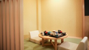 Una habitación pequeña y acogedora con una mesa redonda de madera preparada para una comida, dos sillas blancas con cojines y un mueble bajo de madera contra la pared.