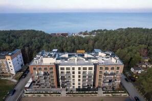 A multi-story building with balconies, a parking area, and a view of the sea.