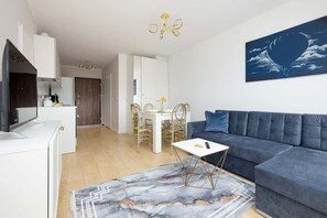 A modern living room with a sofa, a coffee table, a dining area with chairs, and a kitchen in the background.