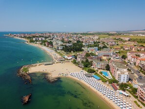 Vista aérea de una ciudad costera con playa, edificios de hotel y un cielo azul despejado.
