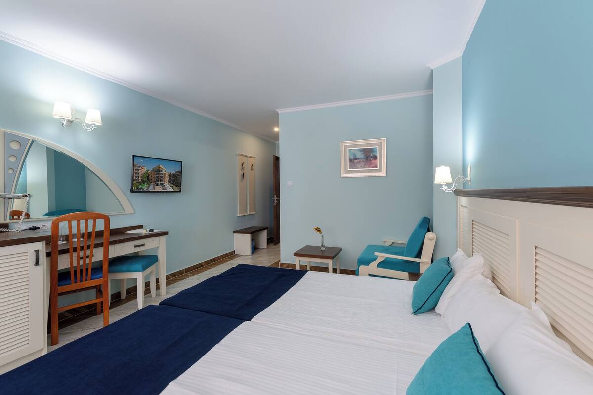 A hotel room with a bed, a desk, a chair, a small table, and a mirror.