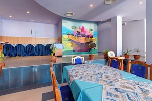 A hotel room with a large mural, a dining area with blue tablecloths, and potted plants. - Evridika (Nessebar)