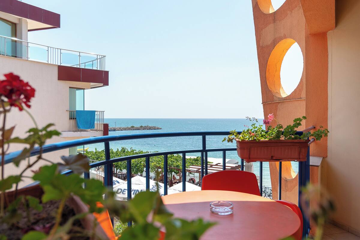 A balcony with a view of the sea, a table, chairs, and potted plants.