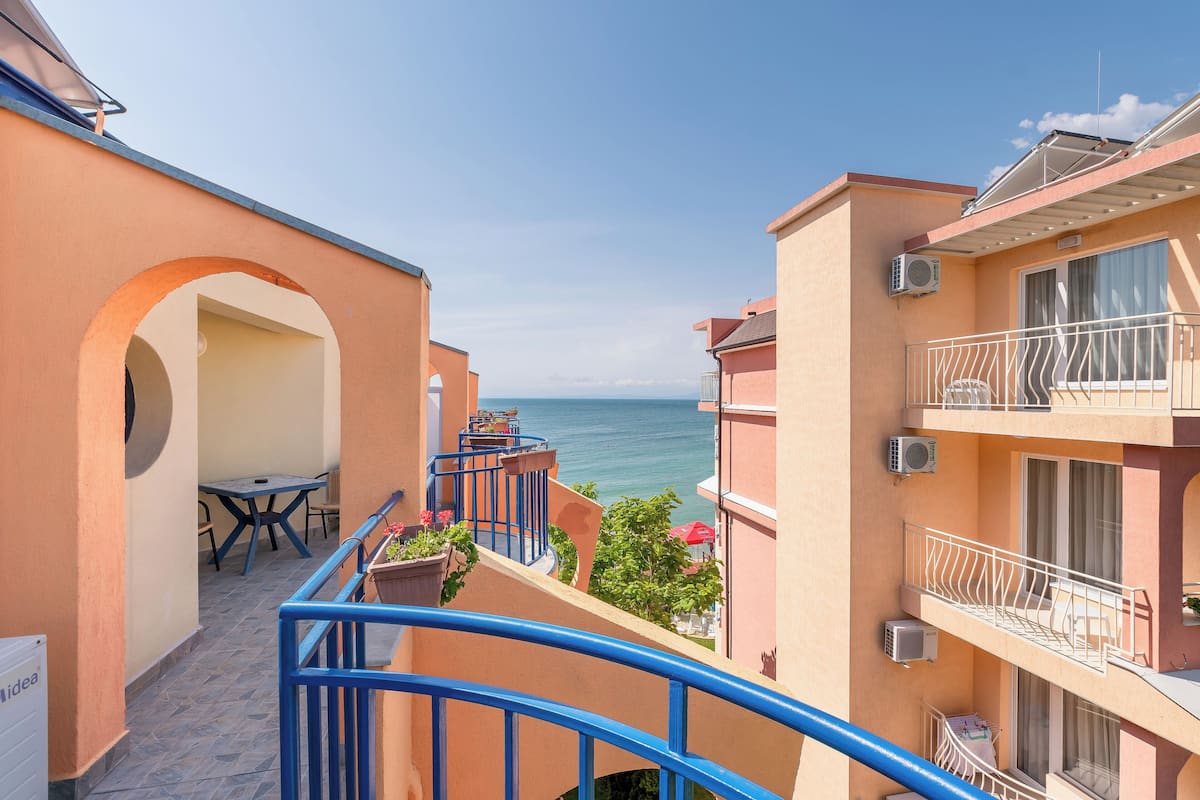 A balcony with a view of the sea, a table with chairs, and a potted plant.