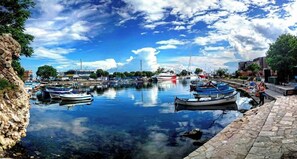 A marina with boats docked, a clear sky, and a stone pathway along the water's edge. - Evridika (Nessebar)