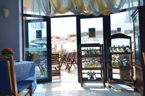 Un restaurant avec une porte vitrée donnant sur l’extérieur, des chaises en bois, une table recouverte d’une nappe bleue et un présentoir à bouteilles.