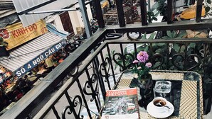 A balcony with a wicker table, a magazine, a vase with flowers, and a railing. - Trang Trang Premium Hotel (Hanoi)