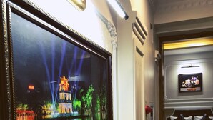 A hotel room with a large flat-screen TV mounted on the wall, a bed with a headboard, a small table, and a door with a handle. - Trang Trang Premium Hotel (Hanoi)