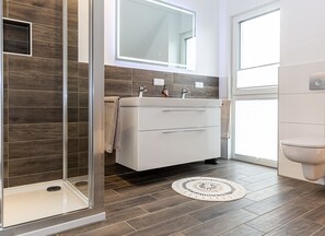 A modern bathroom with a glass shower enclosure, a white sink with a mirror above, and a toilet.