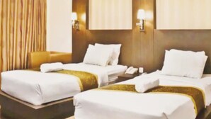 Une chambre d’hôtel avec deux lits, chacun agrémenté de draps blancs et de touches dorées, d’une tête de lit en bois et d’un rideau sur le côté gauche.