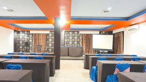 Une salle de conférence avec des rangées de tables et de chaises, un grand écran et un pupitre.
