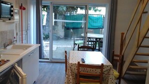 Eine kompakte Küche mit Spüle und Schränken, ein Essbereich mit Tisch und Stühlen sowie eine Glastür, die auf eine Terrasse im Freien mit Tisch und Stühlen führt.
