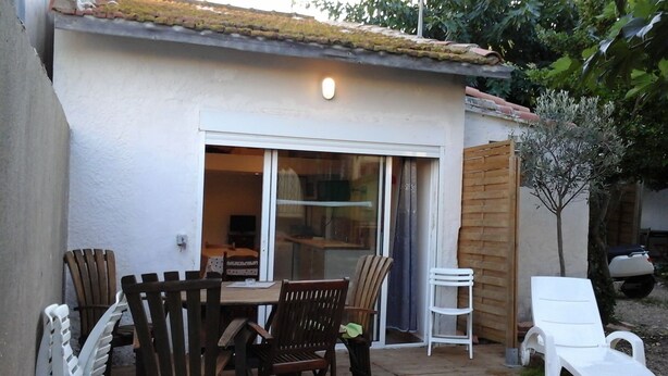 Eine Terrassenfläche mit Tisch und Stühlen, eine Glastür zum Innenbereich und ein kleiner Baum.