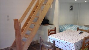Ein Schlafzimmer mit einem Bett, einem Tisch mit puntiertem Tischläufer, einem Holzstuhl, einem kleinen Schreibtisch mit einem Radio und einer Holztreppe.
