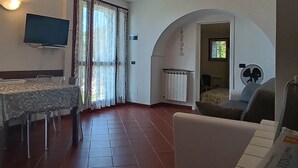 A room with a dining table, chairs, a TV, a radiator, a fan, and an arched doorway.