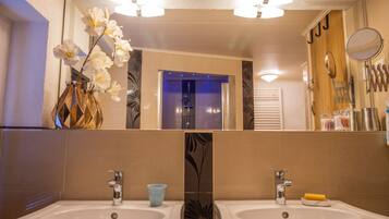 A bathroom with two sinks, a mirror, and a vase with white flowers.