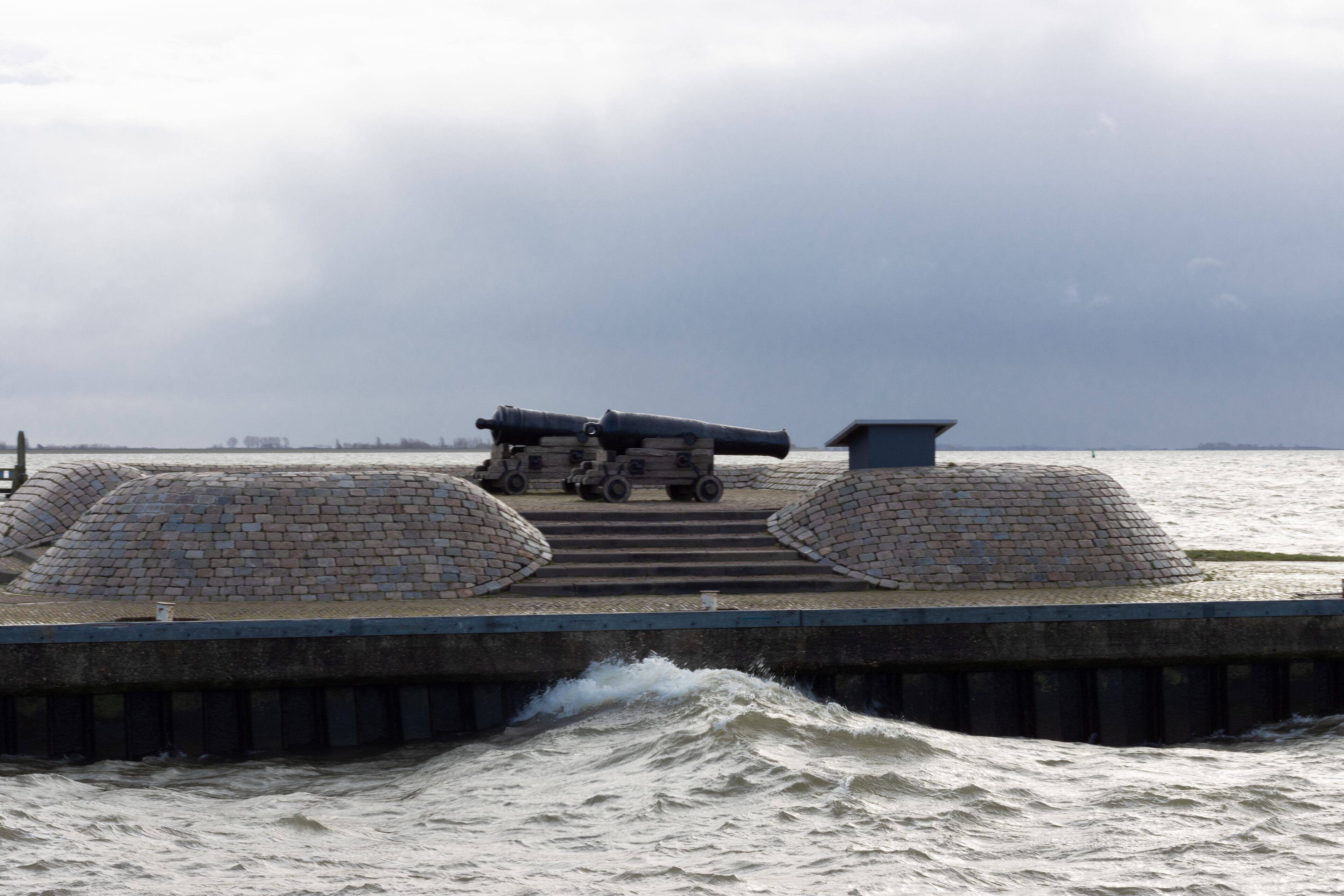 A waterfront promenade with cannons and a brick wall.