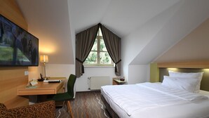 A hotel room with a bed, a desk, a chair, a television, and a window with curtains. - Landhotel Schnuck (Schneverdingen)