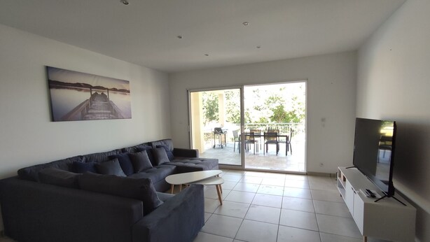Una sala moderna con un sofá oscuro, un televisor de pantalla plana y un ventanal corredero que da a un patio exterior.