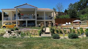 Un edificio de dos pisos con un balcón en el nivel superior, un patio techado y un jardín cuidado con diversas plantas y flores.