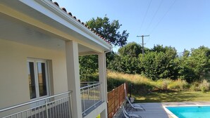 Zona junto a la piscina con terraza de madera, baranda metálica y vista a un paisaje verde.