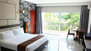 Quarto de hotel moderno com cama grande, escrivaninha e varanda com vista para o verde.