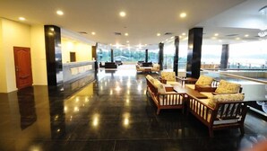 Um hall amplo com piso lustroso, área de estar com sofás e poltronas, e janelas grandes que oferecem uma vista.