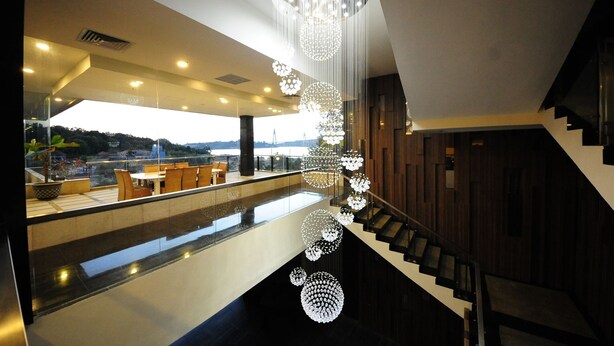 Um hall de hotel moderno com guarda-corpo de vidro, com vista para uma área de refeições e uma escadaria com um lustre único.